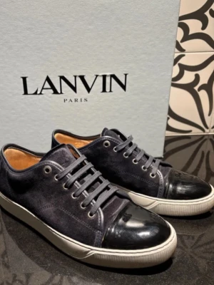 Lanvin svarta sneakers i mocka - Snygga svarta sneakers från Lanvin med ovandel i mocka och glansig tå i skinn. Klassisk låg modell med snörning och vit sula. Perfekta för dig som vill ha en stilren och lyxig look.