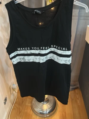 Svart ärmlös linnetopp med tryck - Svart ärmlös linnetopp från New Casual med vitt tryck och texten 'MAKES YOU FEEL SPECIAL' över bröstet. Toppen har två vita ränder framtill och en rund halsringning. Perfekt för en avslappnad och trendig look.