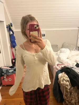 Vit långärmad topp med knappar - Säljer en vit långärmad topp från Gina Tricot med knappar framtill och lätt rynkad effekt. Toppen har en feminin, något figurnära passform och rundad halsringning. Perfekt att styla med jeans eller kjol. Den är i M men man kan reglera hur tajt den ska sitta under bysten med hjälp av snören.