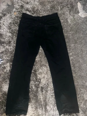 Svarta straight jeans från Levi's - Säljer ett par svarta Levi's jeans i klassisk straight modell. Jeansen har fem fickor, knappgylf och raka ben. Perfekta till en avslappnad stil och funkar året runt. Materialet är slitstarkt denim i bomull.