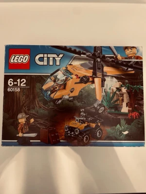 LEGO City Djungel Helikopter 60158 - LEGO City set 60158 Djungel Helikopter innehåller en gul och svart helikopter, en fyrhjuling, minifigurer och tillbehör som skattkista och machete. Perfekt för äventyr i djungelmiljö och kreativa bygglekar! Boxen är lite skadad men allt innehållet är oöppnat och beskrivningarna är med. 