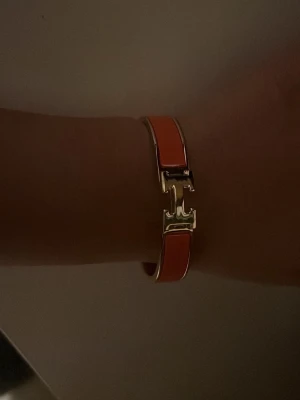 H armband orange - Säljer ett H armband i orange emalj med guldfärgade metalldetaljer. 