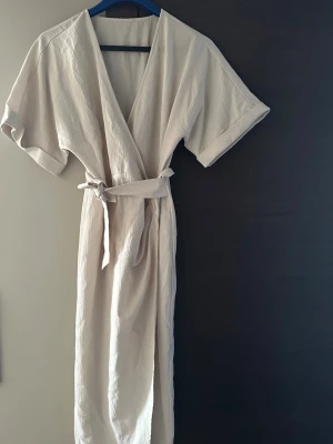 Beige omlott klänning  - Snygg beige midi klänning med knytskärp i midjan och vida, korta ärmar. Tillverkad i ett mjukt, strukturerat bomullstyg som känns skönt mot huden.💕