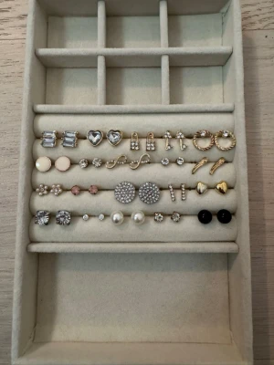 Mixade örhängen i guld och silver - Säljer 20 par örhängen i olika former och färger, inklusive hjärtan, pärlor, stenar, cirklar och bågar. Färgerna är främst guld, silver, vitt och svart. Materialen ser ut att vara metall och pärlimitation. Perfekt för dig som vill variera din stil. OBS köp alla för 150kr eller 11kr/par💐🫶🏼 Oanvända!