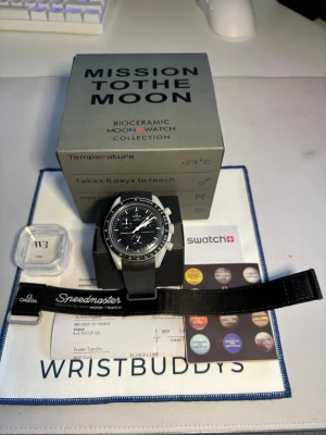 Omega x Swatch MoonSwatch Mission to the Moon - Snygg Omega x Swatch MoonSwatch Mission to the Moon med svart urtavla, vita detaljer och svart biokeramiskt armband. Klockan har kronograf och tydliga index, inspirerad av klassiska Speedmaster. Levereras med originalbox, extra band och certifikat. Det extra gummibandet är ifrån wristbuddy, klockan är köpt 2022 men bytte batteriet här om dagen. Det sitter även ett skyddsplast vilket gör att det inte är en enda repa under plasten på ”glaset”. Det går att köpa klockan utan gummibandet för 2850kr.