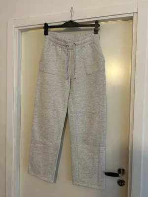Grå mjukisbyxor med snörning - Snygga ljusgrå mjukisbyxor med raka ben och bred resår i midjan. Byxorna har snörning framtill och stora fickor både fram och bak. Perfekta för chill dagar eller när du vill vara extra bekväm.