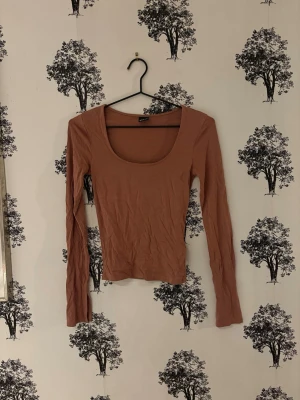 Ljusbrun långärmad topp - En enkel och stilren ljusbrun topp med lång ärm och rund, djup urringning. Tillverkad i mjukt bomullsmaterial som sitter tight mot kroppen. Perfekt att matcha med jeans eller kjol för en clean look. En söm har gått upp vid u-ringningen fram! Se sista bilden!🥰❤️