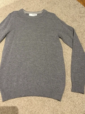 Grå stickad tröja från Selected - Klassisk grå stickad tröja från Selected med rund halsringning och ribbade muddar vid ärmslut och nederkant. Enkel och stilren design som passar till det mesta. Tillverkad i mjukt material för skön känsla.