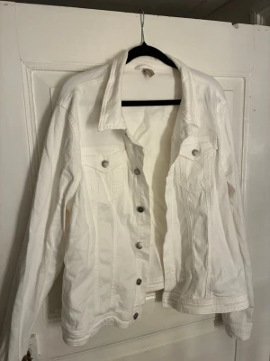 Vit jeansjacka från Soyaconcept - Stilren vit jeansjacka från Soyaconcept med klassisk krage, silverfärgade knappar och två bröstfickor. Jackan har lång ärm och är tillverkad i ett mjukt denimtyg som ger en fräsch och clean look. Perfekt att slänga över en hoodie eller t-shirt. Storlek XXL men passar M/L/XL beroende på hur tight man vill ha den.