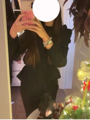 Svart volangblus med puffärm XXS  - Snygg svart blus med volangdetaljer och puffiga axlar. Blusen har lång ärm och en figurnära passform som ger en trendig siluett. Perfekt att styla med både jeans och kjol för en cool look.