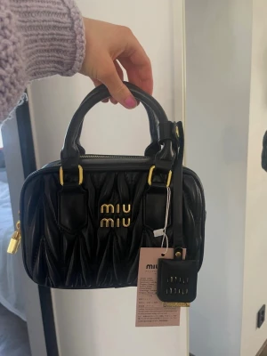 Skitsnygg Svart quiltad handväska från Miu Miu!! - Snygg svart handväska från Miu Miu i quiltad skinn med guldfärgade detaljer och logga framtill. 💕Väskan har dubbla handtag, dragkedja upptill och medföljande tag. Perfekt storlek för det viktigaste och ger en lyxig touch till din outfit. SÅ SNYGG!!🤩🤩🤩Oandvänd, säljer för att jag har för många väskor💖