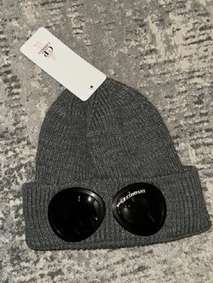 Mörkgrå stickad mössa  - Snygg mörkgrå stickad mössa från  med klassisk ribbstickad design och uppvikt kant. Perfekt accessoar för kyliga dagar och enkel att matcha med olika outfits.