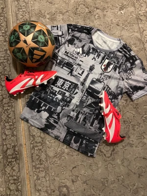 Tokyo-inspirerad sporttröja - Säljer en kortärmad sporttröja med svartvitt Tokyo-motiv och grafiska tryck. Tröjan är tillverkad i ett lätt och snabbtorkande material, perfekt för fotboll eller träning. Snygg och unik design som sticker ut på planen.