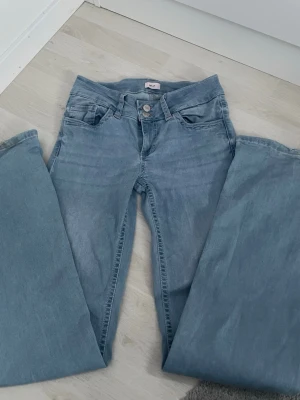 Nelly Jeans - Jag säljer ett par ljusblå bootcut jeans med rosa söm på bakfickan. Klassisk femficksmodell och normal passform. Perfekta för dig som gillar bootcut jeans! De är lite slitna längst ner men inget märkvärdigt.