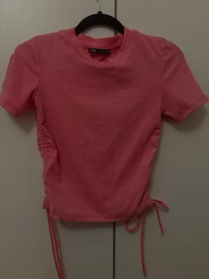 Rosa ribbad topp från Zara - Trendig rosa ribbad topp från Zara med korta ärmar och snörning i sidorna för en snygg croppad look. Perfekt till jeans eller kjol och enkel att styla för en cool vardagsoutfit.