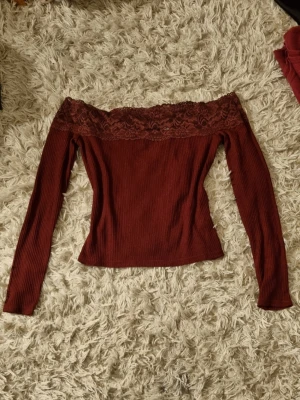 Bordeaux offshoulder topp med spets - Trendig bordeauxfärgad offshoulder topp med långa ärmar och vacker spetsdetalj upptill. Ribbad struktur ger en snygg passform och toppen är perfekt för dig som vill sticka ut. Snygg att matcha med både jeans och kjol.