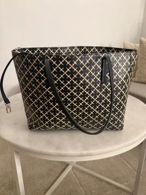 Svart shoppingväska med mönster - Väska från by malene Birger, fläckar inuti och lite som lossnat uppe på väskan som ni ser på bilderna. Annars är banden osv i bra skick