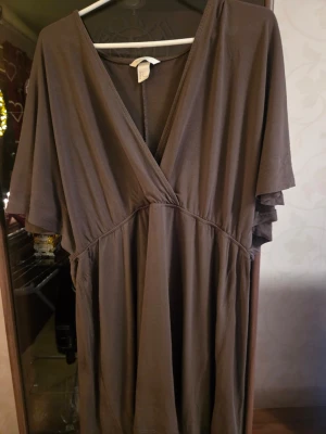 Brun omlottklänning med v-ringning - Mjuk brun klänning i bomull med omlott-design och djup v-ringning. Klänningen har korta ärmar och ett avslappnat fall som ger en loose passform. Perfekt för dig som gillar enkel och stilren look.Färg: Khaki!.