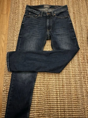 Mörkblå jeans från Dressmann - Snygga mörkblå jeans från Dressmann med klassisk femficksdesign och raka ben. Jeansen har subtila slitningar och kontrastsömmar som ger en stilren look. Perfekta för dig som gillar en tidlös och enkel stil.