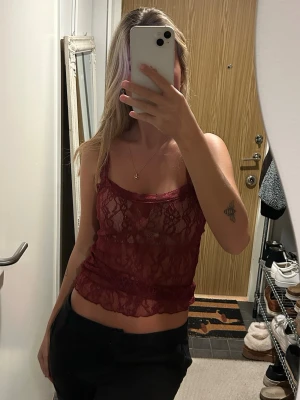 Vinröd spetsbody med smala axelband - Säljer en vinröd topp i genomskinlig spets och smala axelband. Modellen är figurnära.