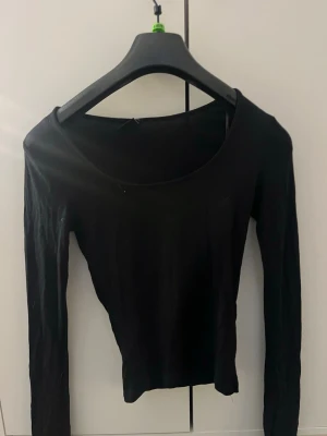 Svart långärmad topp - En enkel svart långärmad topp med rund halsringning. Perfekt att styla med jeans eller kjol för en clean look. Tunn och mjuk i materialet, passar året runt.