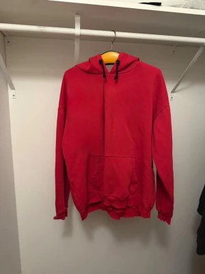 Röd hoodie med magficka - Enkel röd hoodie med huva och dragsnören. Har en stor magficka framtill och ribbade muddar vid ärmslut och nederkant. Perfekt för en avslappnad stil och passar till det mesta. Materialet känns mjukt och bekvämt.