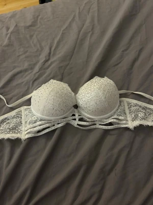 Vit spets-bh med vadderade kupor - Säljer en vit bh med vadderade kupor och vacker spetsdetalj över hela bh:n. Axelbanden är justerbara och ryggen har dekorativa band och spets. Knappt använd 🤍Storlek:B