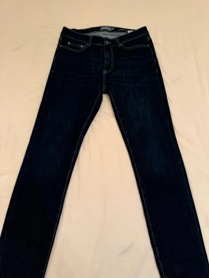 Dressmann Jeans Slim - Snygga mörkblå jeans i slim fit och klassisk femficksdesign. Jeansen har kontrastsömmar och en enkel look som passar till allt. Tillverkade i ett mjukt bomullsmaterial för skön känsla hela dagen.