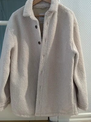 Beige teddyjacka från Zara - Mysig beige teddyjacka från Zara i relaxed fit. Jackan har krage, knappar framtill och är tillverkad i mjukt teddy-material som ger en chill och trendig look. Perfekt för lager på lager under kyliga dagar.