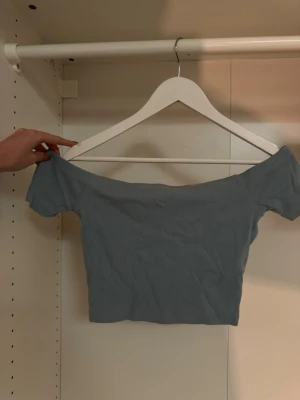 Ljusblå offshoulder topp Bik Bok - Trendig ljusblå offshoulder topp från Bik Bok i ribbad bomullsmix. Croppad modell med korta ärmar och stretchig passform som sitter snyggt på kroppen. Perfekt att styla med höga jeans eller kjol för en cool look💙