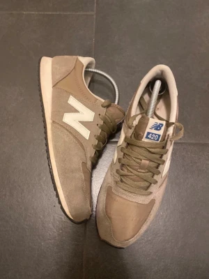 Beige New Balance 420 sneakers - Säljer ett par snygga beige New Balance 420 sneakers med klassisk vit N-logga på sidan. Skorna har snörning, rund tå och platt sula. Materialet är en mix av mocka och syntet, vilket ger en stilren och bekväm känsla.