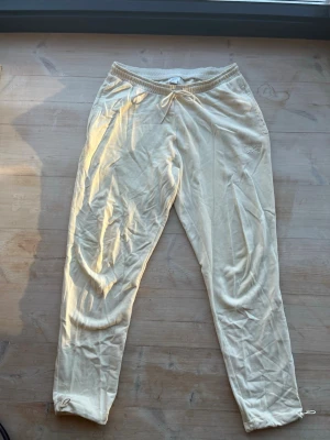Benvita mjukisbyxor från Reebok strl L - Säljer ett par beiga mjukisbyxor från Reebok med dragsko i midjan och avslappnad passform. Tillverkade i mjukt bomullsmaterial, perfekta för chill dagar. Klassisk design utan mönster och med elastisk midja för extra komfort.