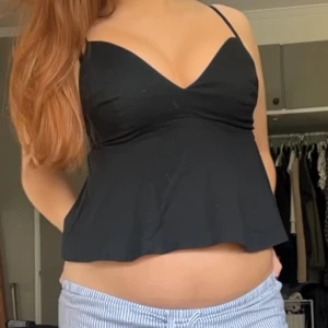 Svart linnetopp med smala axelband - Snygg svart linnetopp med smala axelband och v-ringad urringning. Toppen har en lätt utsvängd passform och ärmlös design, perfekt för varma dagar eller som ett lagerplagg. Enkel och stilren look som passar till mycket.