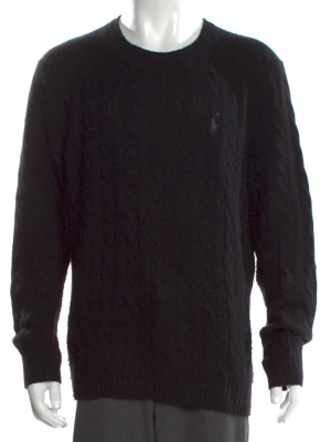Svart kabelstickad tröja Polo Ralph Lauren - Kabelstickad svart tröja från Polo Ralph Lauren med rund halsringning och diskret broderad logga på bröstet. Tröjan har långa ärmar och ribbade muddar vid ärmslut och nederkant. Perfekt för dig som gillar klassisk och stilren look.