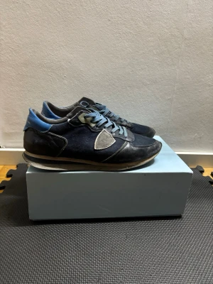 Philippe Model blå sneakers herr - Snygga sneakers från Philippe Model i olika blå nyanser med grå detaljer och snörning. Skorna har en klassisk låg siluett, rund tå och är tillverkade i en mix av mocka och textil. Perfekta för dig som gillar stilrena och sportiga sneakers.