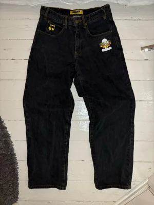 Svarta baggy jeans från Butter - Svarta baggy jeans från Butter med broderade detaljer. Jeansen har kontrastsömmar i gult och en avslappnad, loose passform.  Lite slitna nedertill som man kan se på bilden