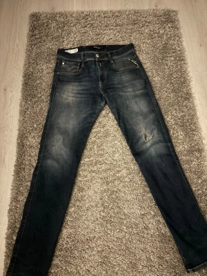 Mörkblå Replay anbass slim jeans - Snygga mörkblå jeans från Replay anbass med klassisk femficksdesign och lite slitningar framtill. Jeansen har smal passform. Storlek 29W 30L