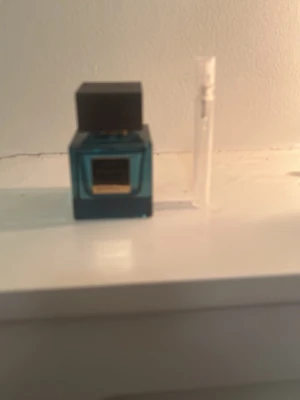 Blå parfymflaska med svart kork rituals  - Snygg parfym i en fyrkantig blå glasflaska med svart fyrkantig kork och guldfärgad etikett framtill. Medföljer även ett litet genomskinligt provrör. Perfekt för dig som gillar stilrena och moderna doftflaskor.