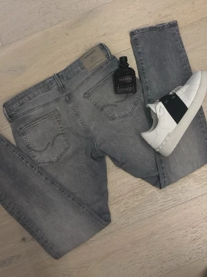 Gråa slim jeans från Jack & Jones - Snygga gråa jeans från Jack & Jones med klassisk femficksmodell och diskreta slitningar. Jeansen har en slim passform och är tillverkade i mjuk bomullsdenim med stretch för extra komfort. Perfekta för en trendig och avslappnad look.