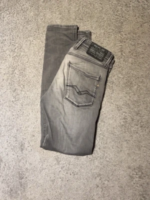 Replay grå jeans  - Snygga grå jeans från Replay med raka ben och klassiska bakfickor med dekorativa sömmar. Jeansen har en mörkare tvätt. Litet hål vid vänster bakficka men inget som syns när man har på dem. Skriv vid minsta fundering.