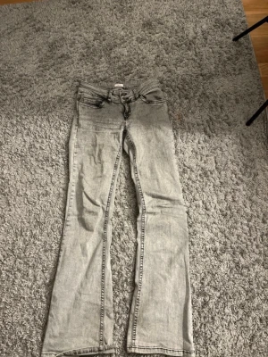 Ljusgrå bootcut jeans med broderi - Säljer ett par ljusgrå bootcut jeans med snyggt broderade bakfickor. Jeansen har klassisk femficksdesign och är tillverkade i mjukt denimtyg. Perfekta för dig som gillar en avslappnad men trendig look. Litet hål i byxan, se bilden.