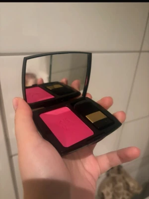 Lancome rosa rouge med spegel - Snyggt rosa rouge från Lancome i en svart kompakt dosa med spegel och tillhörande borste. Rouget har en intensiv rosa nyans och kommer i ett elegant etui med gulddetalj på borsten. Perfekt för att ge kinderna en fräsch färg.