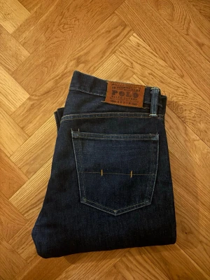Mörkblå jeans från Polo Ralph Lauren - Snygga mörkblå jeans från Polo Ralph Lauren med klassisk femficksdesign och raka ben. Jeansen har en läderpatch med logga bak i midjan och kontrastsömmar. Perfekta till en clean och stilren look.