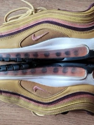 Nike Air Max 97 guld sneakers - Nike Air Max 97 sneakers i guld med röda detaljer och synlig luftbubbla i sulan. Skorna har en vågig design med inslag av svart och vitt, samt snörning och rund tå. Perfekta för dig som vill sticka ut med en ikonisk och sportig look.  ( SLITAGE PÅ HÅLARNA  SYNS KNAPAST MED SKORNA PÅ) ska tvätta dessa innan ut skcik
