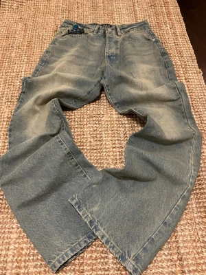 Blå flared fited jeans med en washed vintage look - Säljer ett par blå jeans med flared fit och snyggt slitna detaljer. Jeansen har klassisk femficksmodell med bra fickor som får plats med mycket småt och gott. Perfekta för dig som gillar en avslappnad och trendig stil.