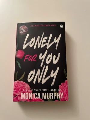 Lonely For You Only av Monica Murphy - En romantisk roman på engelska med svart omslag, stora vita och rosa bokstäver och blommotiv. Boken handlar om Scarlett Lancaster och en oväntad romans med en musiker. Perfekt för dig som gillar kärlekshistorier och drama.