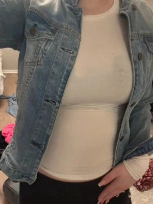 Blå croppad jeansjacka - Snygg blå croppad jeansjacka med klassisk knappstängning och bröstfickor. Jackan har en normal passform och är perfekt att slänga över en t-shirt för en avslappnad look.