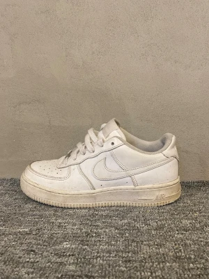 Nike Air Force 1 vita sneakers - Nike Air Force 1 sneakers i helvitt med klassisk låg siluett och rund tå. Skorna har snörning, perforerad tåbox och platt sula med Air-dämpning 