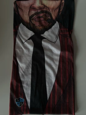 Halsvärmare med gangster motiv - Cool halsvärmare med tryck av en svart slips och vit skjorta, samt röda och svarta ränder. Perfekt accessoar för att sticka ut i skidbacken eller när man fiskar.