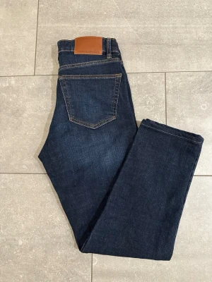 Mörkblå jeans från These Glory Days - Snygga mörkblå jeans från These Glory Days med klassisk femficksdesign och kontrastsömmar. Jeansen har rak passform och är tillverkade i slitstarkt bomullsdenim. Perfekta för en clean och stilren look. Stl 29/32 men är förkortade, innebenslängd är 71cm. Aldrig använda!